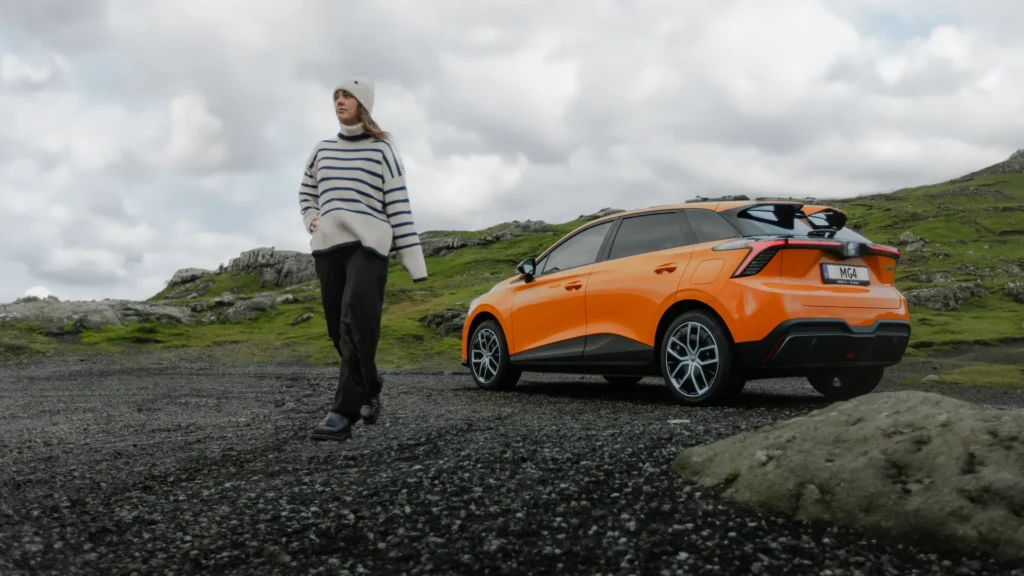 Person i stripete genser ved oransje bil på steinete bakke.