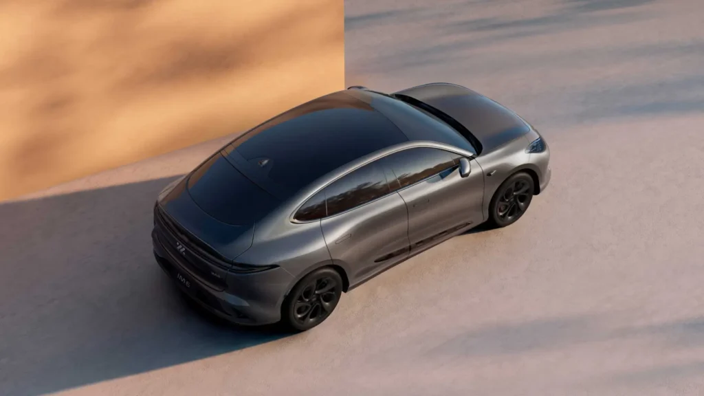 Sølvfarget elbil parkert ved lys vegg, sett ovenfra.