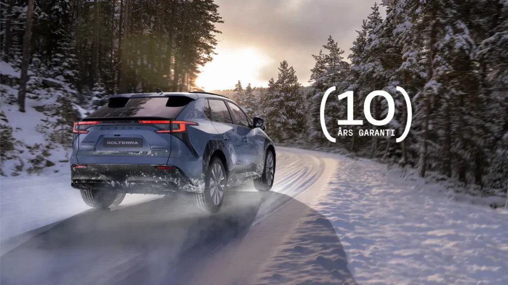 Blå Subaru Solterra på snødekt vei ved solnedgang, tekst: "10 års garanti".